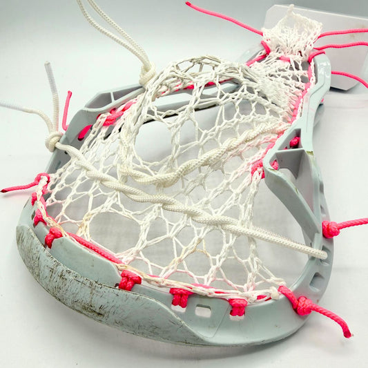 A lacrosse head with a white mesh net and bright pink laces, photographed on a clean white background.