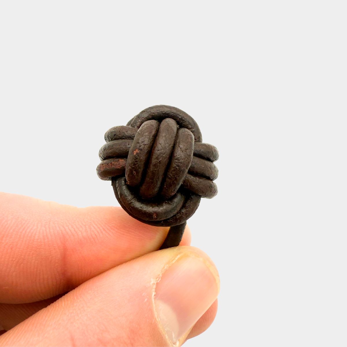Monkey’s Fist Chocolate knot held between fingers against a light gray background